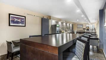 Um lobby de hotel moderno com um balcão de recepção extenso, área de estar e cozinha ao fundo.