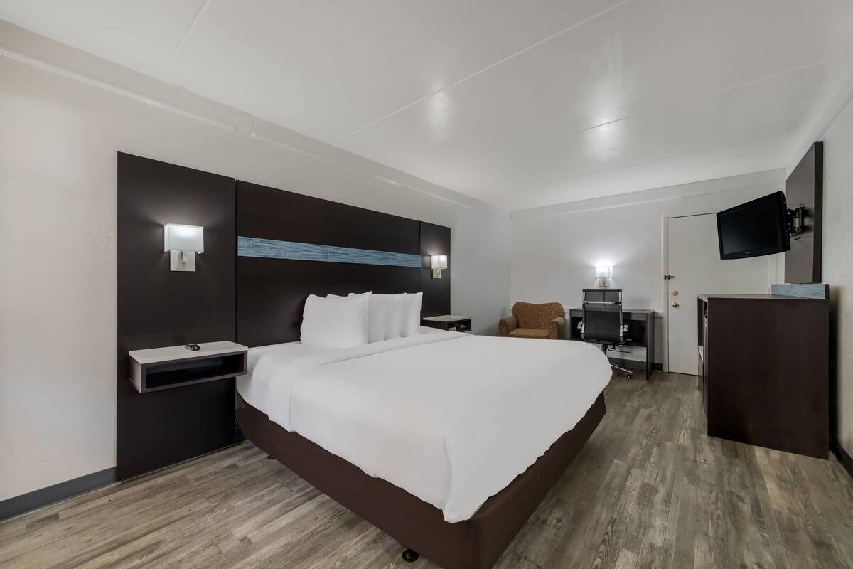 Ein modernes Hotelzimmer mit einem großen Bett, Nachttischen, einem Flachbildfernseher, einem Schreibtisch und einem Sessel.