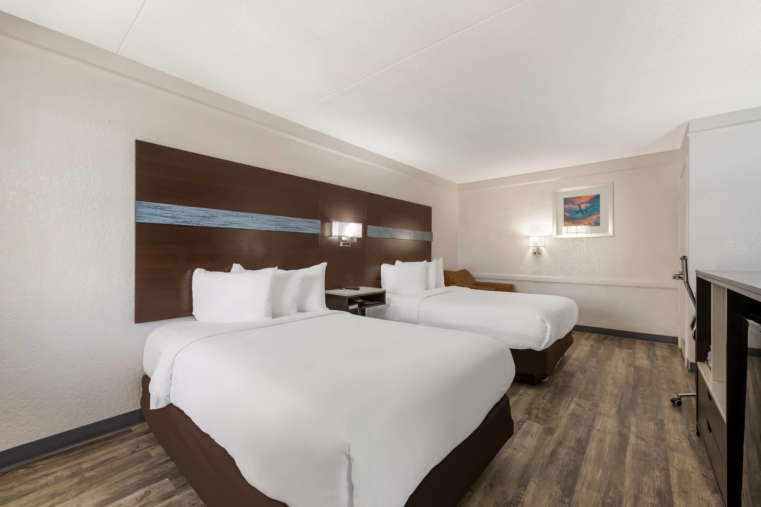 Habitación de hotel con dos camas, cabecero de madera, mesita de noche, escritorio y un pequeño cuadro en la pared.