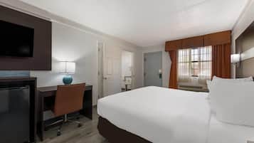 A hotel room with a bed, desk, chair, TV, lamp, and a window with curtains.