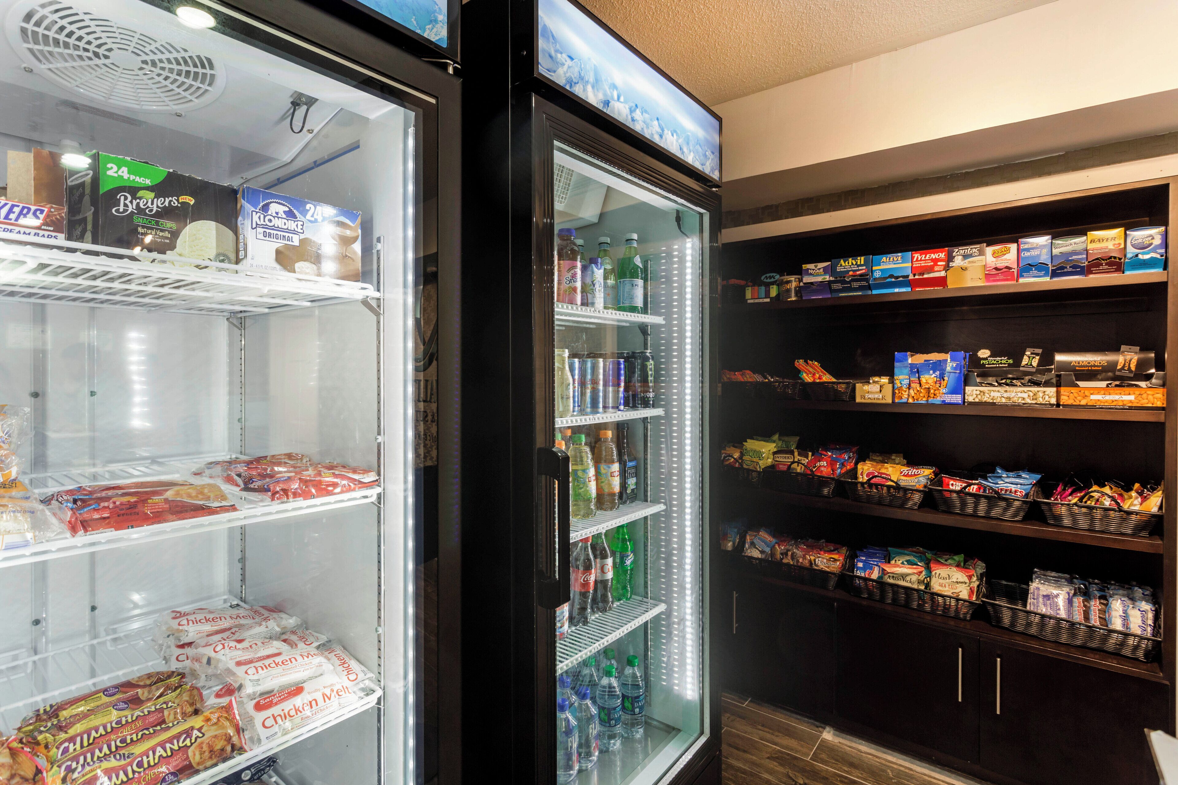 A refrigerator stocked with beverages and snacks, and adjacent shelves with packaged goods.