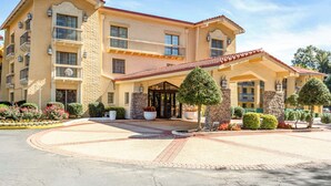 Un hotel de varios pisos con entrada central, balcones y un patio ajardinado.