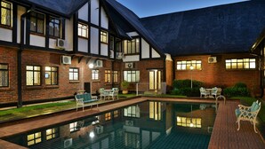 A traditional building with a swimming pool, outdoor seating, and a brick facade. - Cresta Churchill (Bulawayo)