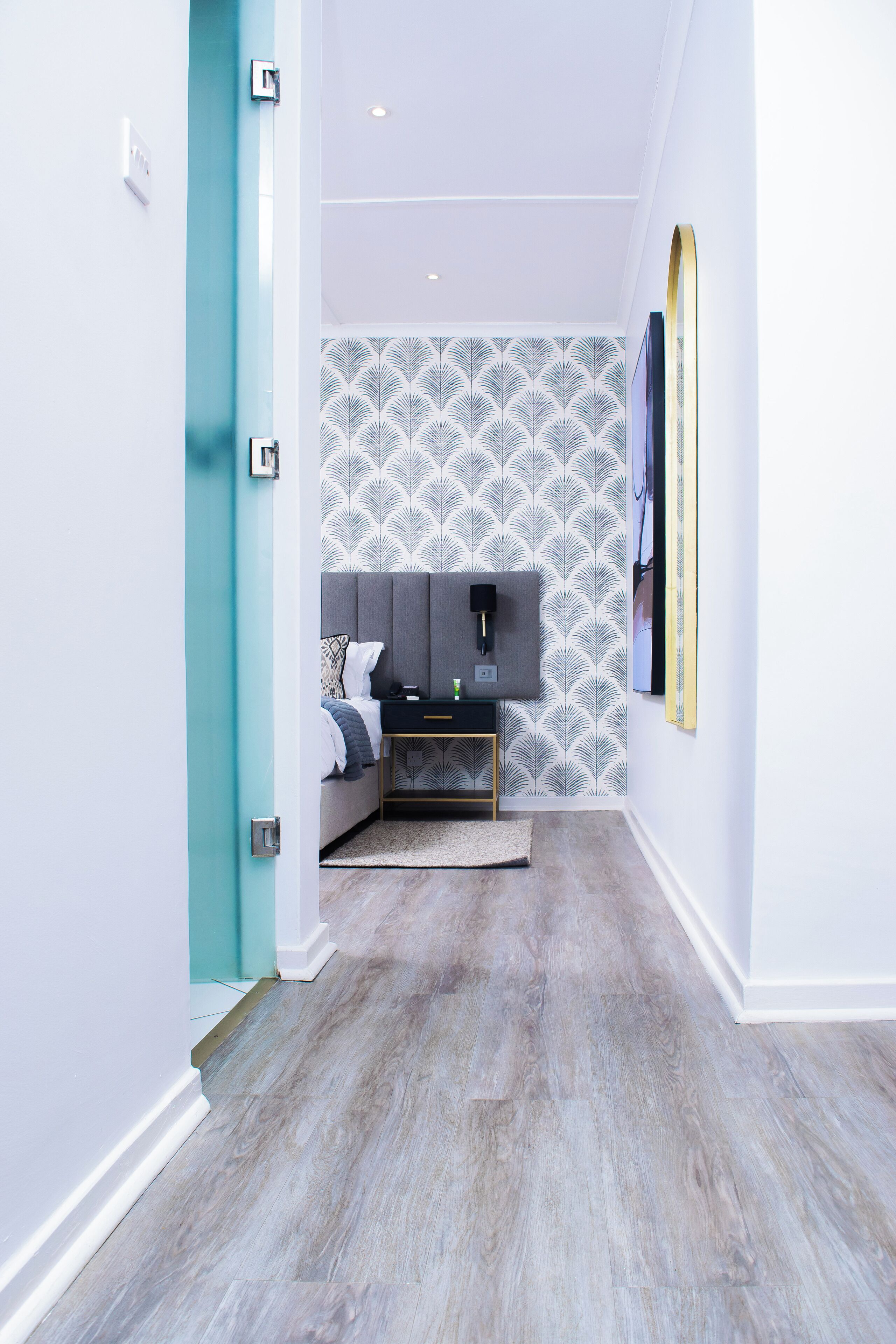 Un dormitorio moderno con cabecera gris, cama con ropa de cama blanca, mesita de noche pequeña y televisor montado en la pared.