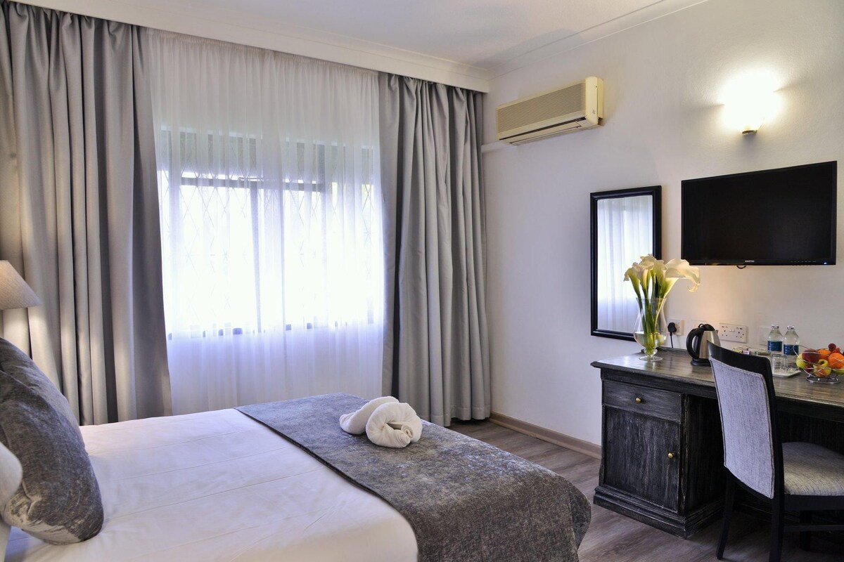 A hotel room with a bed, a desk, a chair, a flat-screen TV, and a window with curtains.