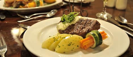 Een bord met steak, aardappelen en groenten, en een glas witte wijn op een tafel.