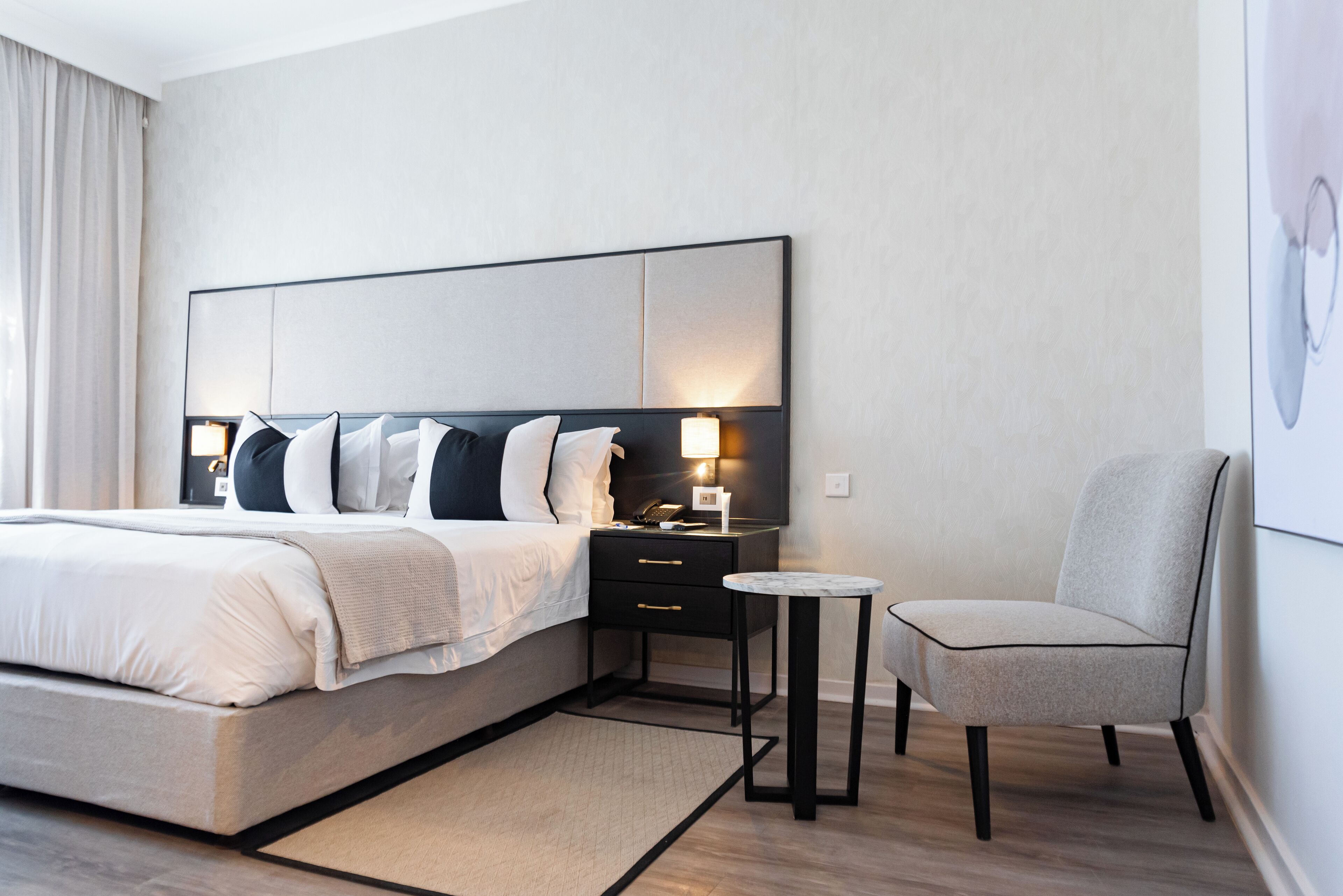 A modern hotel room with a large bed, bedside tables, a chair, and a small table.