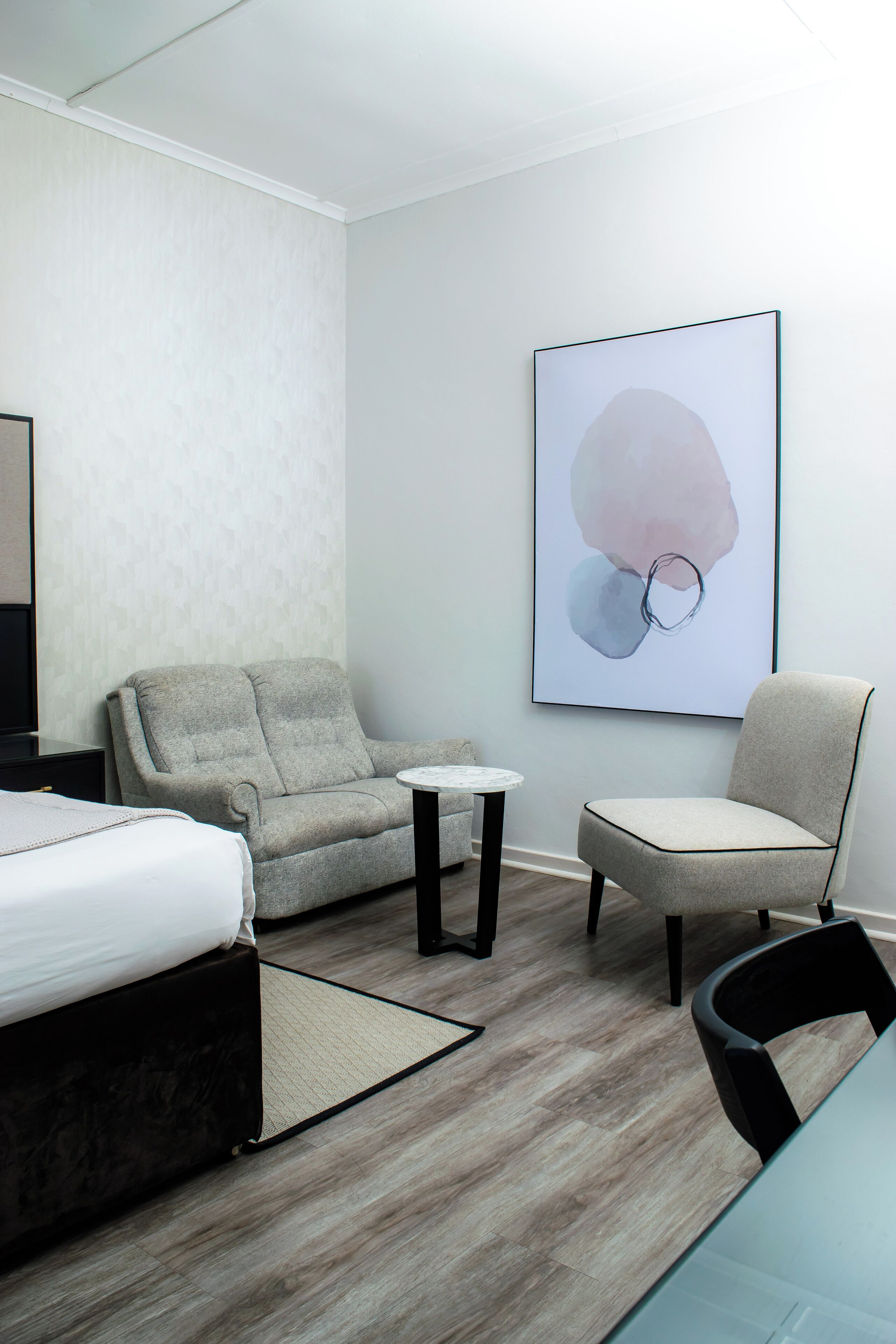 Een moderne hotelkamer met een bed, twee fauteuils, een klein rond tafeltje en een groot abstract schilderij aan de muur.