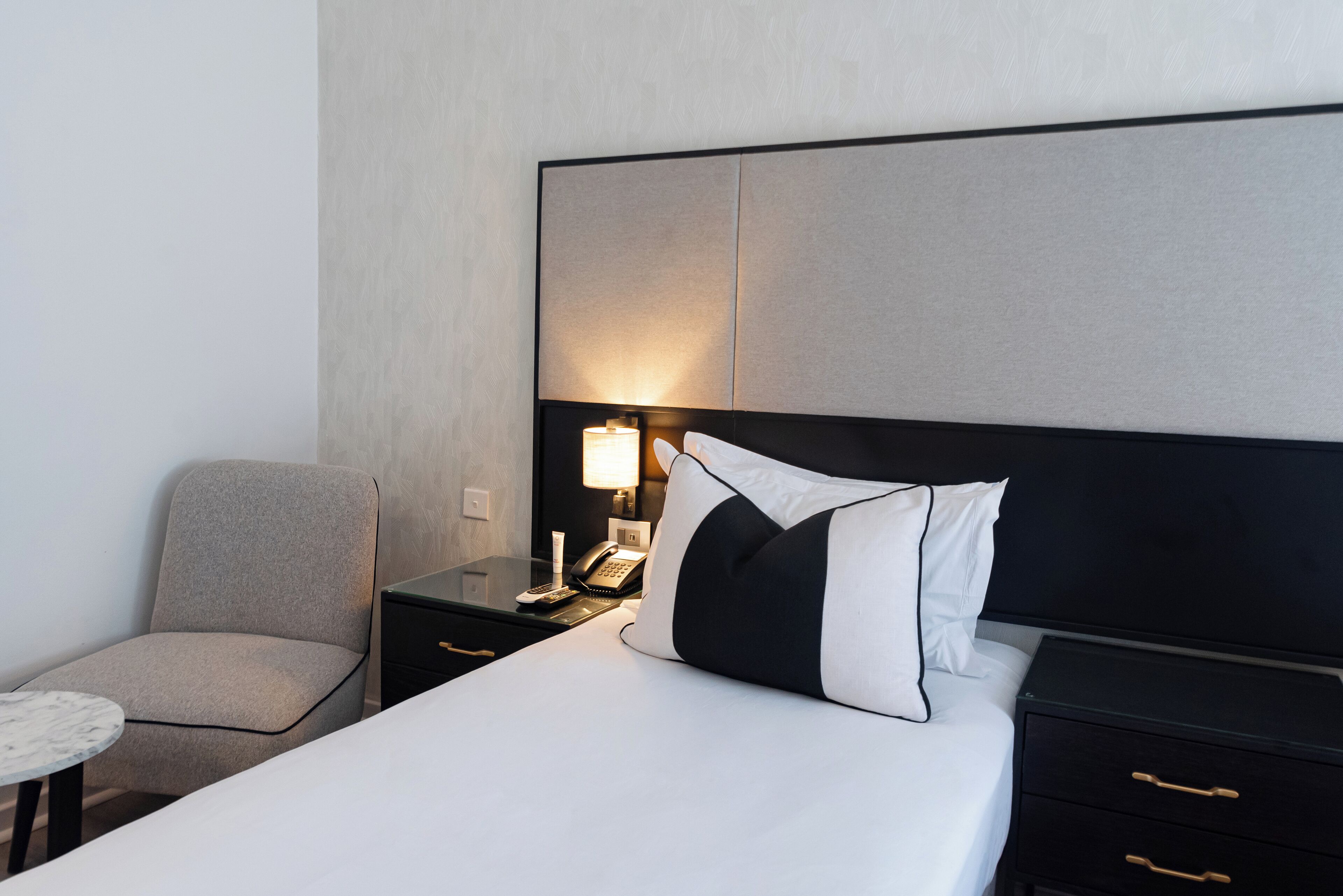 Een hotelkamer met een bed, een stoel, een nachtkastje met een lamp en een telefoon.