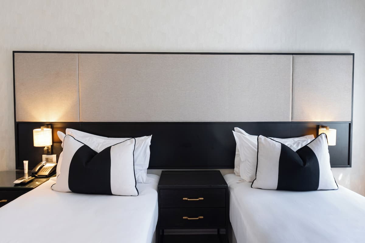 A hotel room with a large bed, two bedside tables with lamps, and a black nightstand with a phone and a lamp.