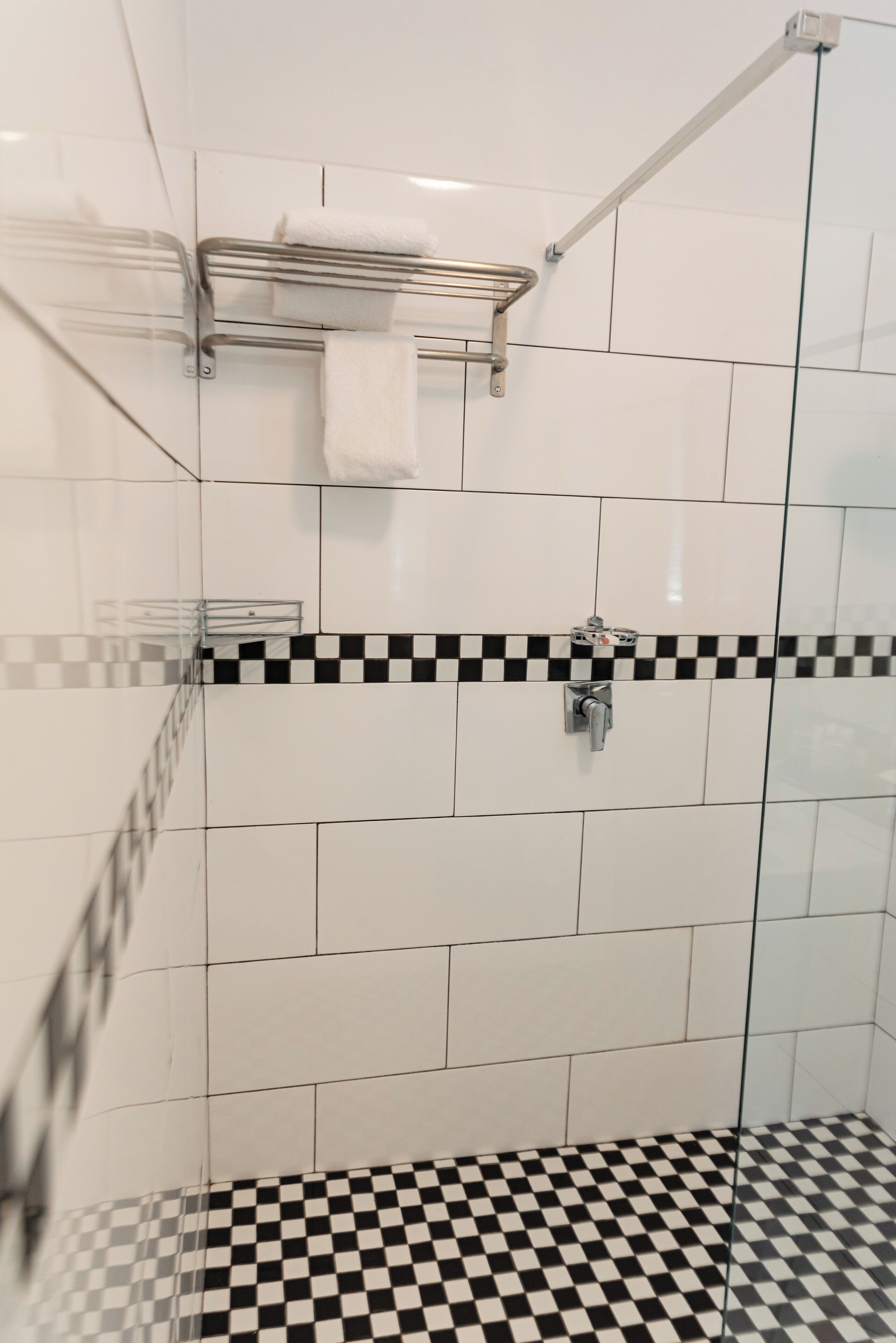 A shower area with a glass door, a metal towel rack, and a checkered floor pattern.
