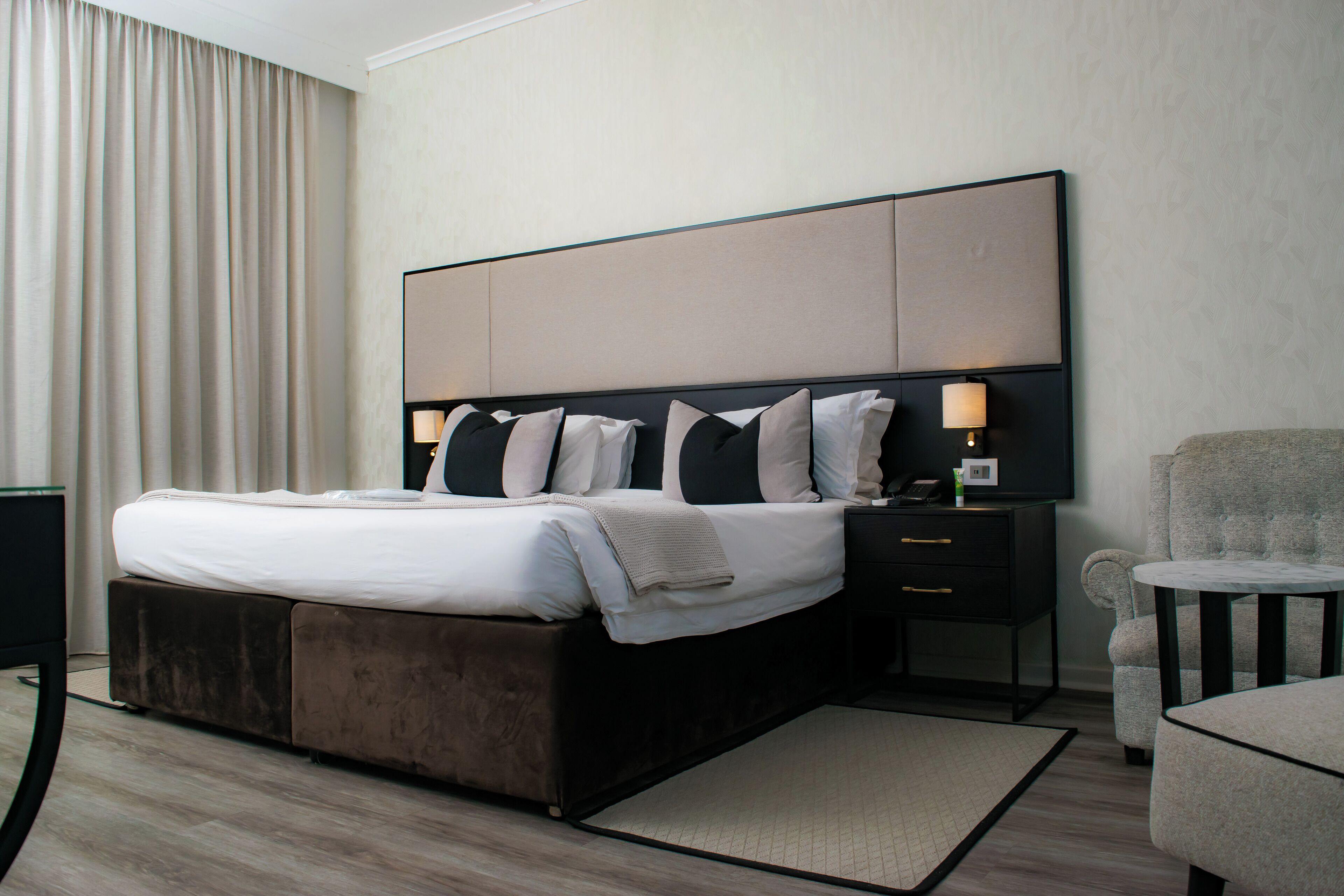 Ein modernes Hotelzimmer mit einem großen Bett, einem Nachttisch mit Lampe, einem Sessel und einem kleinen Tisch.