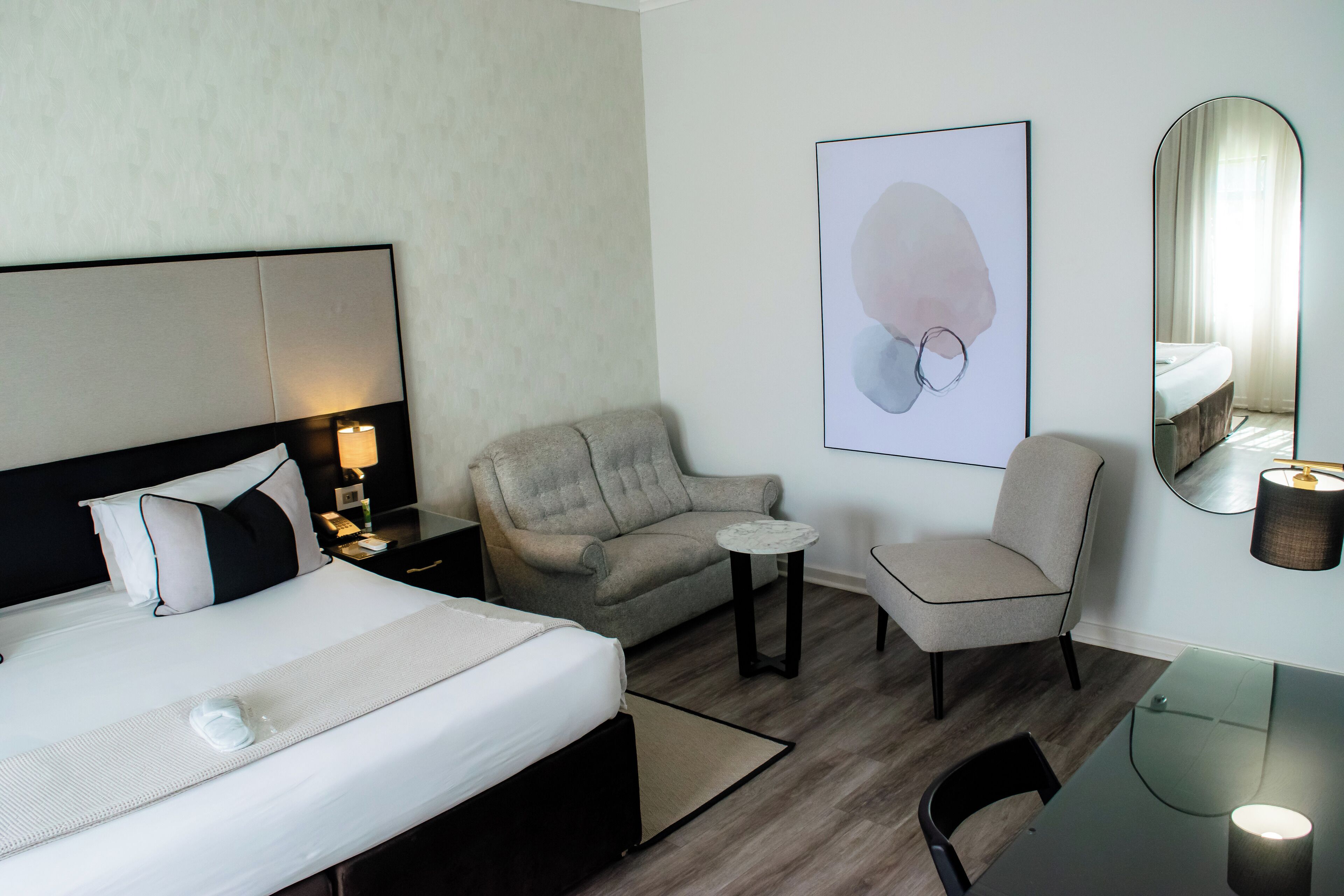A hotel room with a bed, a sofa, a small table, a chair, a desk, and a mirror.
