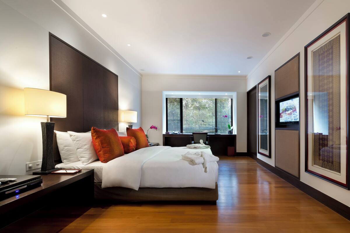 Habitación de hotel moderna con una cama grande, lámparas de noche, un escritorio con computadora y un televisor en la pared.