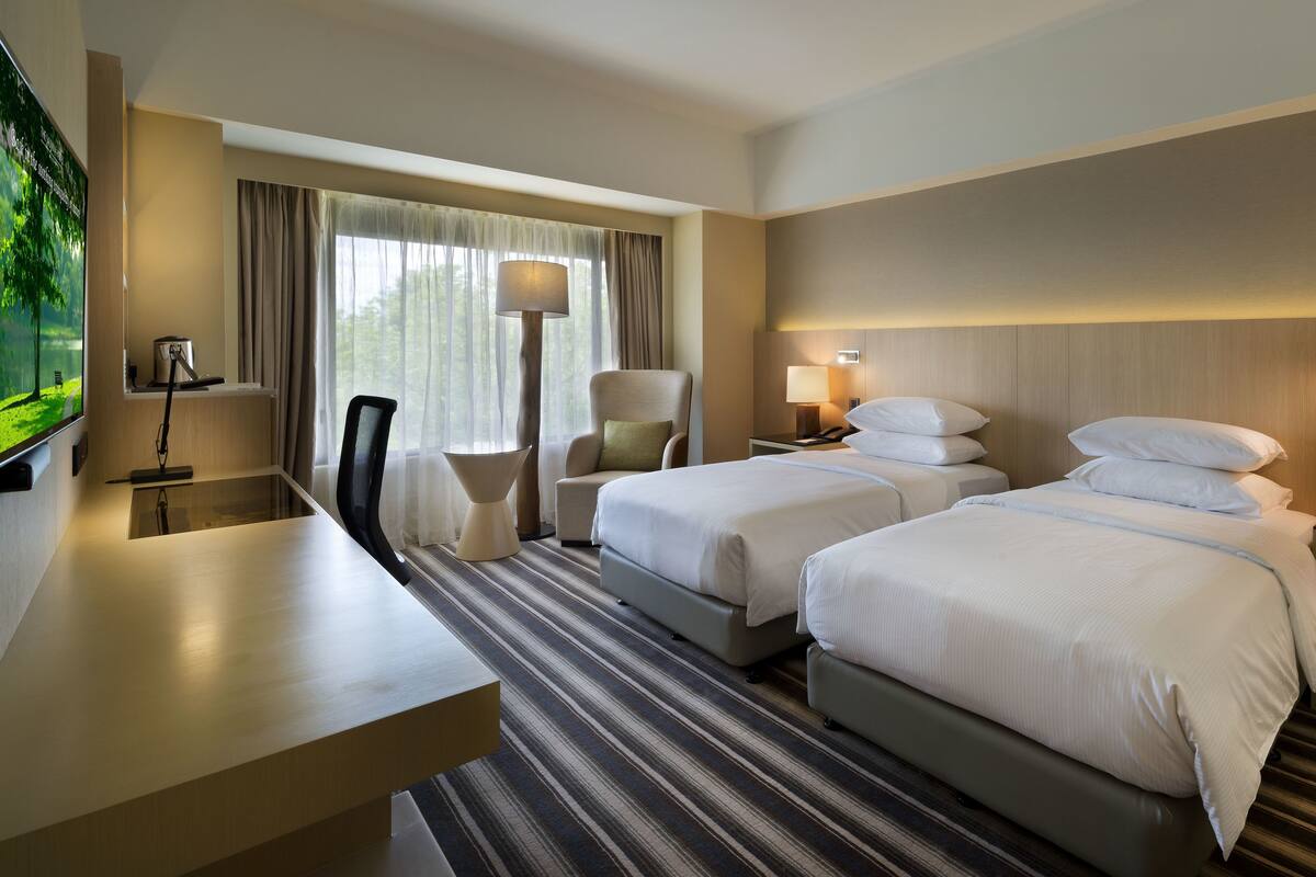 Habitación de hotel con dos camas, un escritorio, una silla, un televisor y una ventana con cortinas.