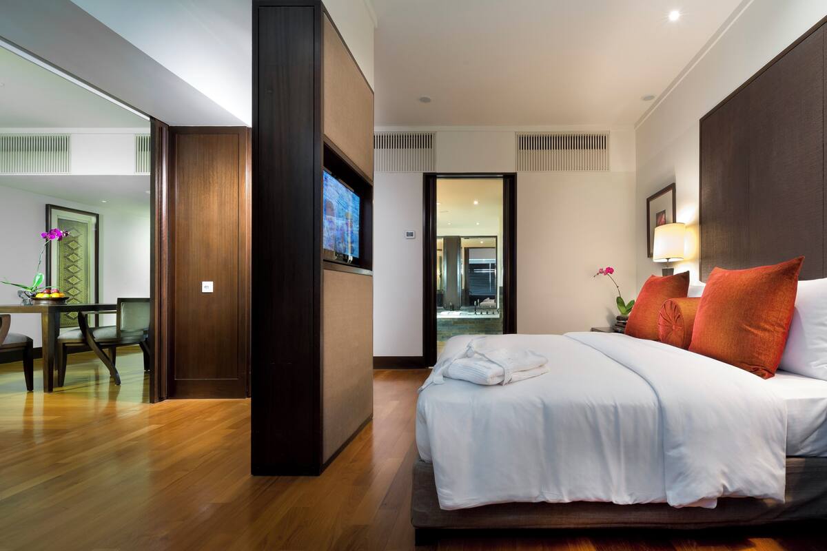 Una habitación de hotel con cama, mesita de noche, lámpara y vista al baño.