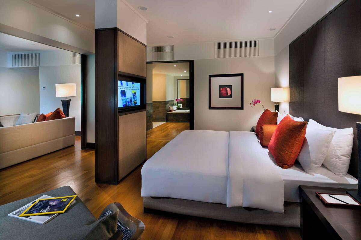 Una habitación de hotel moderna con una cama grande, mesitas de noche, un televisor y un espacio de descanso con un sofá y sillón.