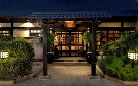 A traditional Japanese-style building with a tiled roof, a wooden gate, and a well-lit entrance.