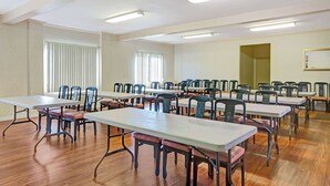 Un salón de conferencias con varias mesas y sillas, ventanas amplias con persianas y un techo con luces fluorescentes.