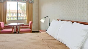 Habitación de hotel con cama, una mesa redonda, dos sillas, una lámpara y una ventana con cortinas.