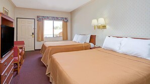 Habitación de hotel con dos camas, televisión, escritorio y ventana con cortinas.