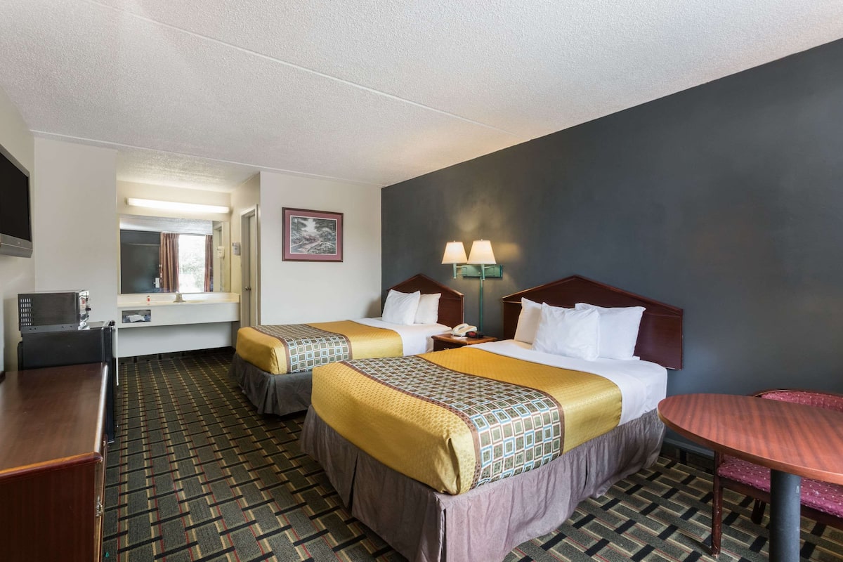 A hotel room with two beds, a desk, a chair, a table, and a TV.