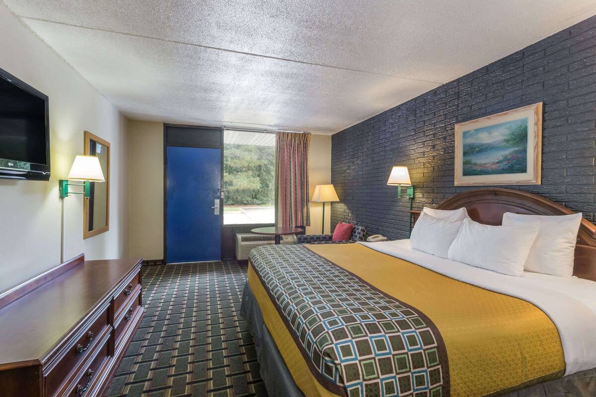 A hotel room with a large bed, a flat-screen TV, a wooden dresser, two bedside lamps, and a painting on the wall.