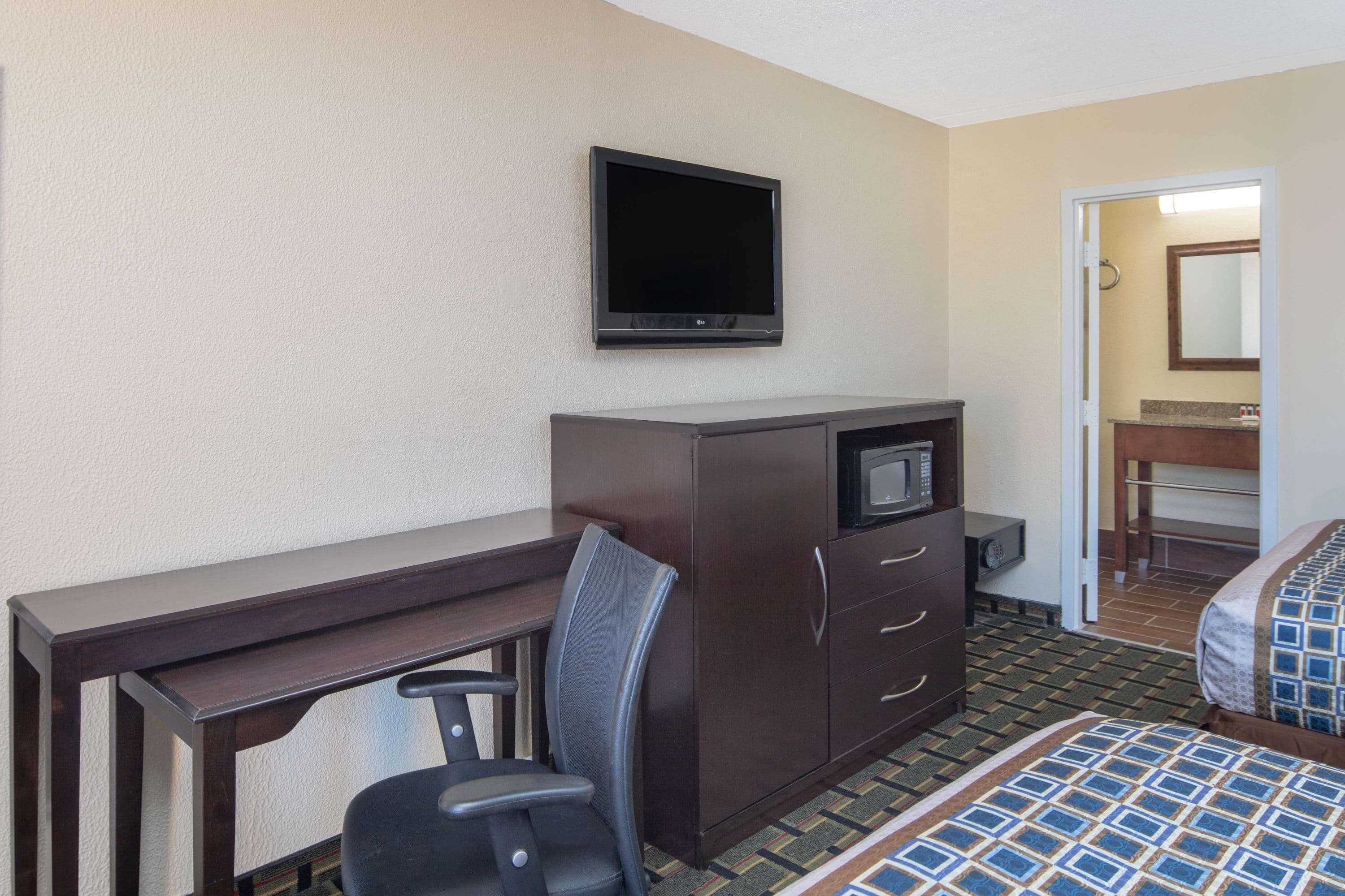 A hotel room with a desk, chair, TV, wardrobe, and a bed.