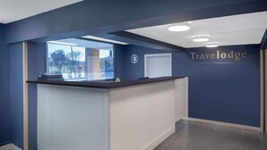 A reception area with a dark blue wall, a reception desk, a clock, and a window offering a view of trees and buildings. - Travelodge by Wyndham Savannah Area/Richmond Hill (Richmond Hill)