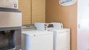 A laundry area with two washing machines and a self-serve laundry sign. - Travelodge by Wyndham Savannah Area/Richmond Hill (Richmond Hill)