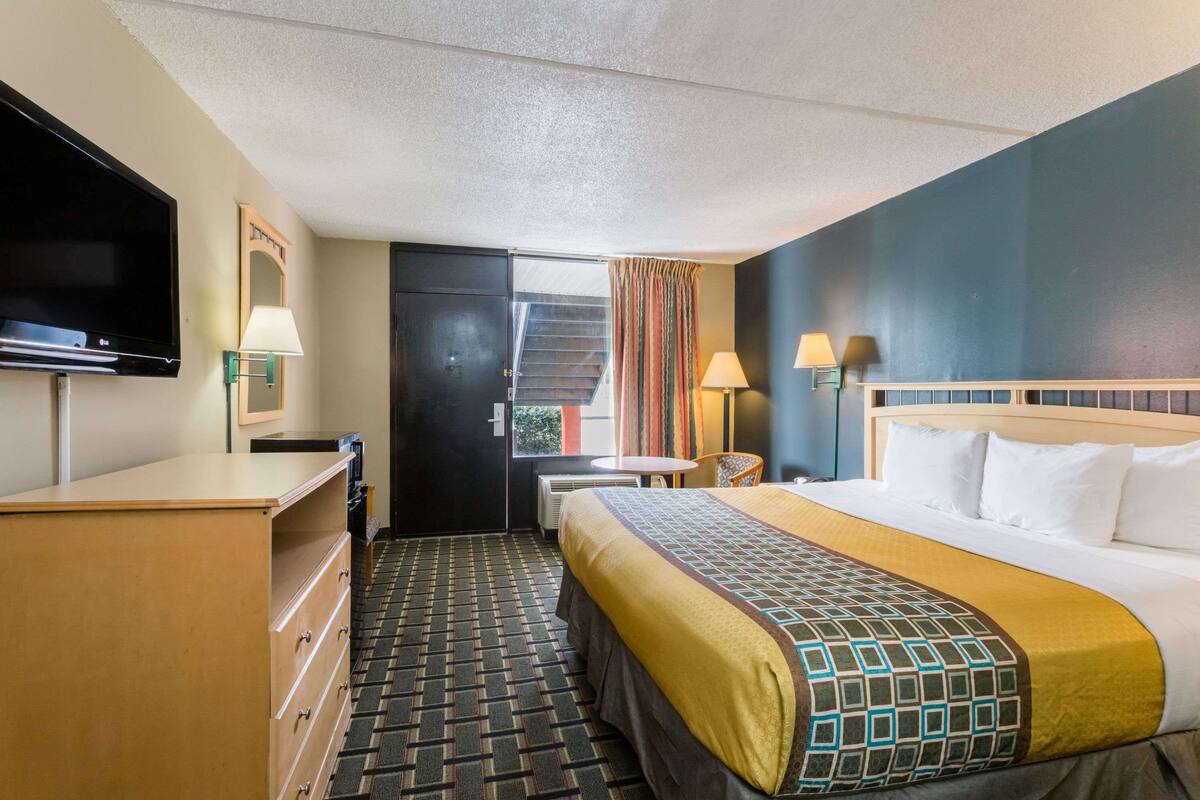 A hotel room with a bed, a desk, a television, a dresser, and a window with curtains.