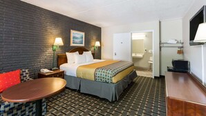 A hotel room with a bed, bedside tables, a desk, and a chair. There is a bathroom visible through an open door. - Travelodge by Wyndham Savannah Area/Richmond Hill (Richmond Hill)