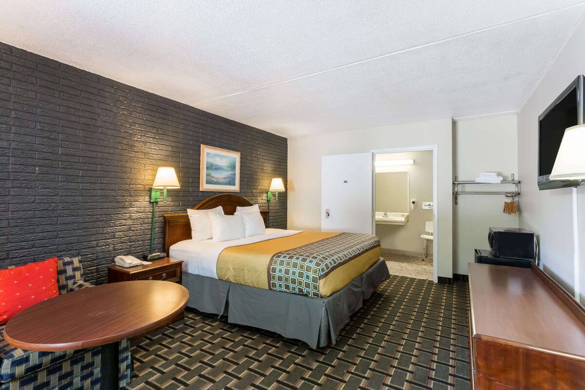 A hotel room with a bed, bedside tables, a desk, and a chair. There is a bathroom visible through an open door.