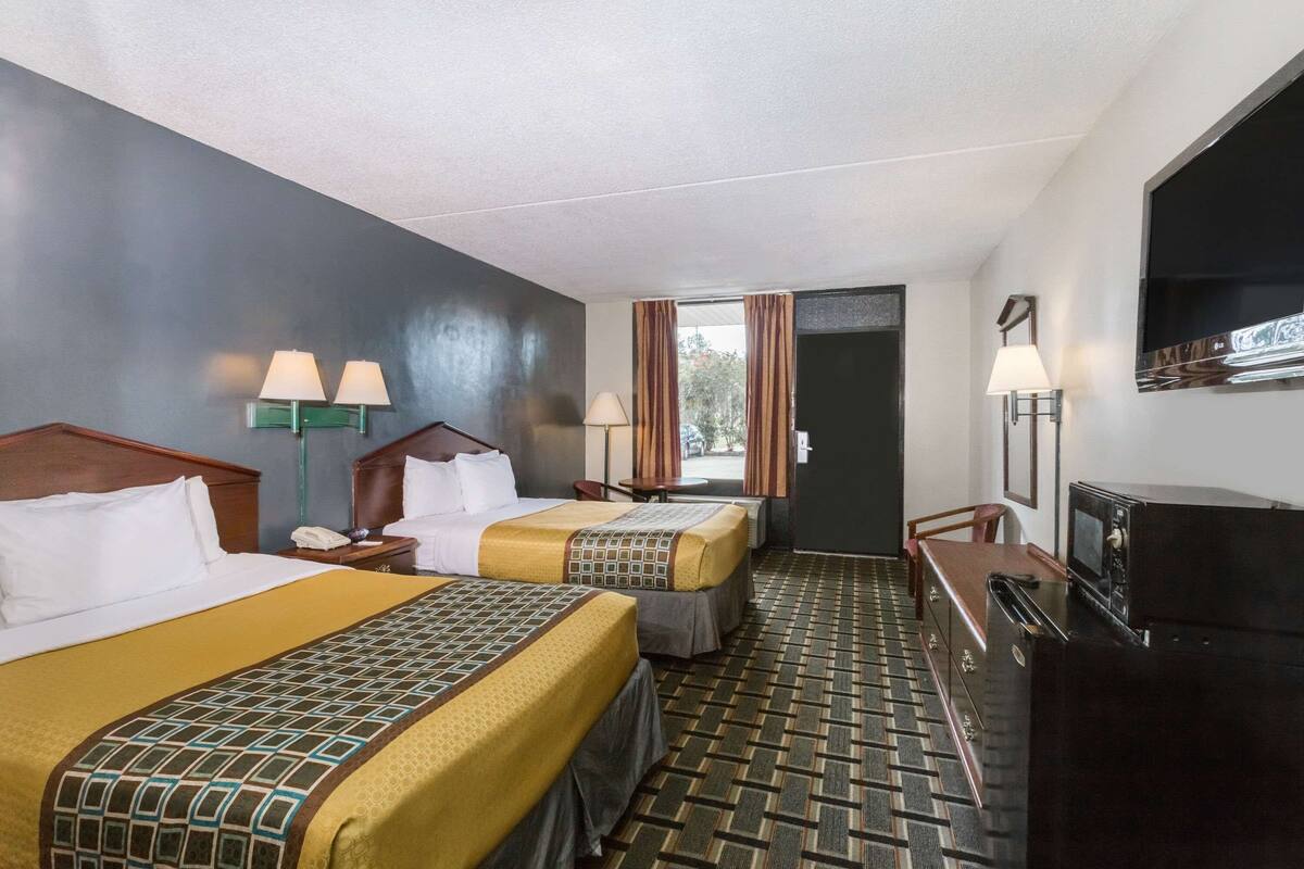 A hotel room with two beds, a TV, a desk, and a window with curtains.
