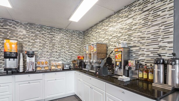A modern kitchen with white cabinets, a granite countertop, and various appliances like a coffee machine and a waffle maker. - Travelodge by Wyndham Savannah Area/Richmond Hill (Richmond Hill)