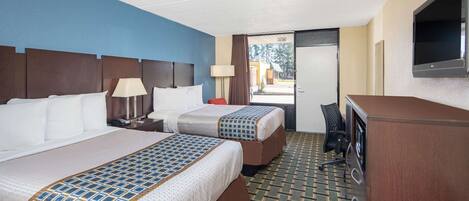 A hotel room with two beds, a TV, a desk, and a view of the outside.