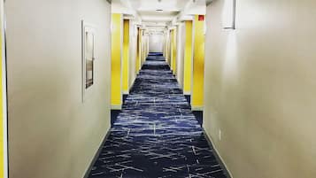 A hotel hallway with a patterned carpet, yellow doors, and a straight layout.