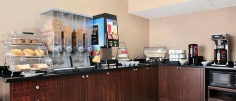 Un mostrador de desayuno autoservicio con una máquina de café, una selección de pasteles y un dispensador de bebidas.