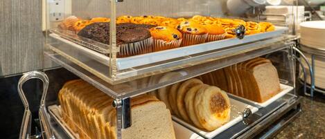 A buffet counter with various baked goods including muffins, cookies, and bread.