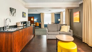 A modern hotel room with a kitchen area, a living room with a sofa and a yellow ottoman, and a dining area. - Comfort Inn & Conference Centre Toronto Airport (Toronto)