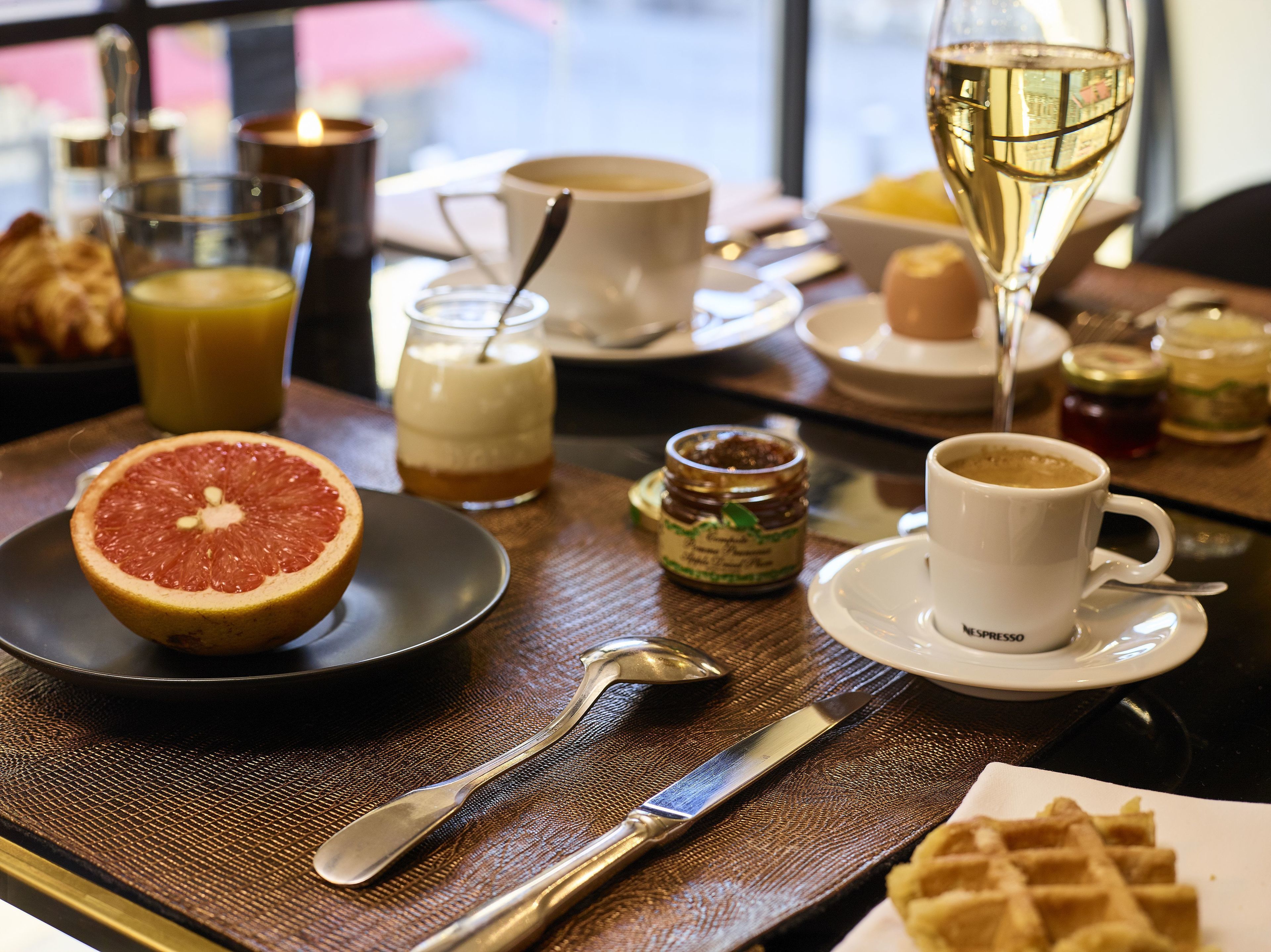 Una mesa de desayuno con pomelo, una taza de café, una copa de vino y diferentes condimentos.