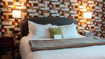 Una cama bien hecha con cabecera, almohadas y manta. Hay mesitas de noche con lámparas y una pared con un diseño geométrico.