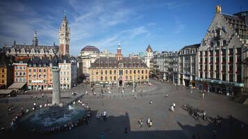 Une place historique avec une fontaine centrale, entourée de bâtiments richement décorés et dominée par un imposant beffroi.