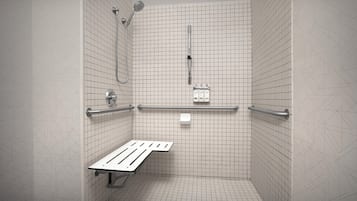 Une petite cabine de douche carrelée, équipée d’un banc, de barres d’appui et d’un pommeau de douche à main.