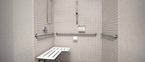 Une petite cabine de douche carrelée, équipée d’un banc, de barres d’appui et d’un pommeau de douche à main.