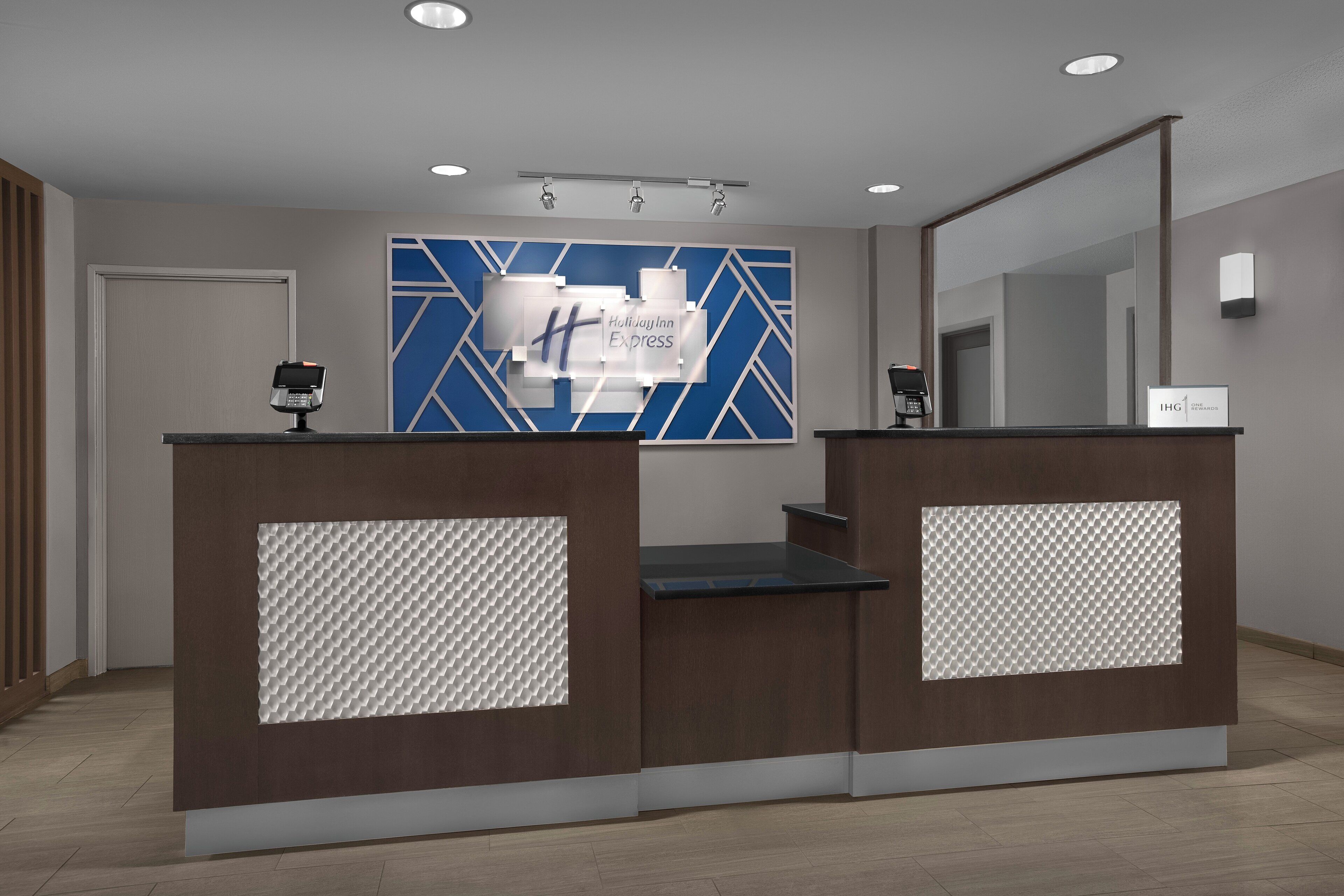 A reception desk with a blue geometric wall design, a Holiday Inn Express sign, and a modern, minimalist interior.