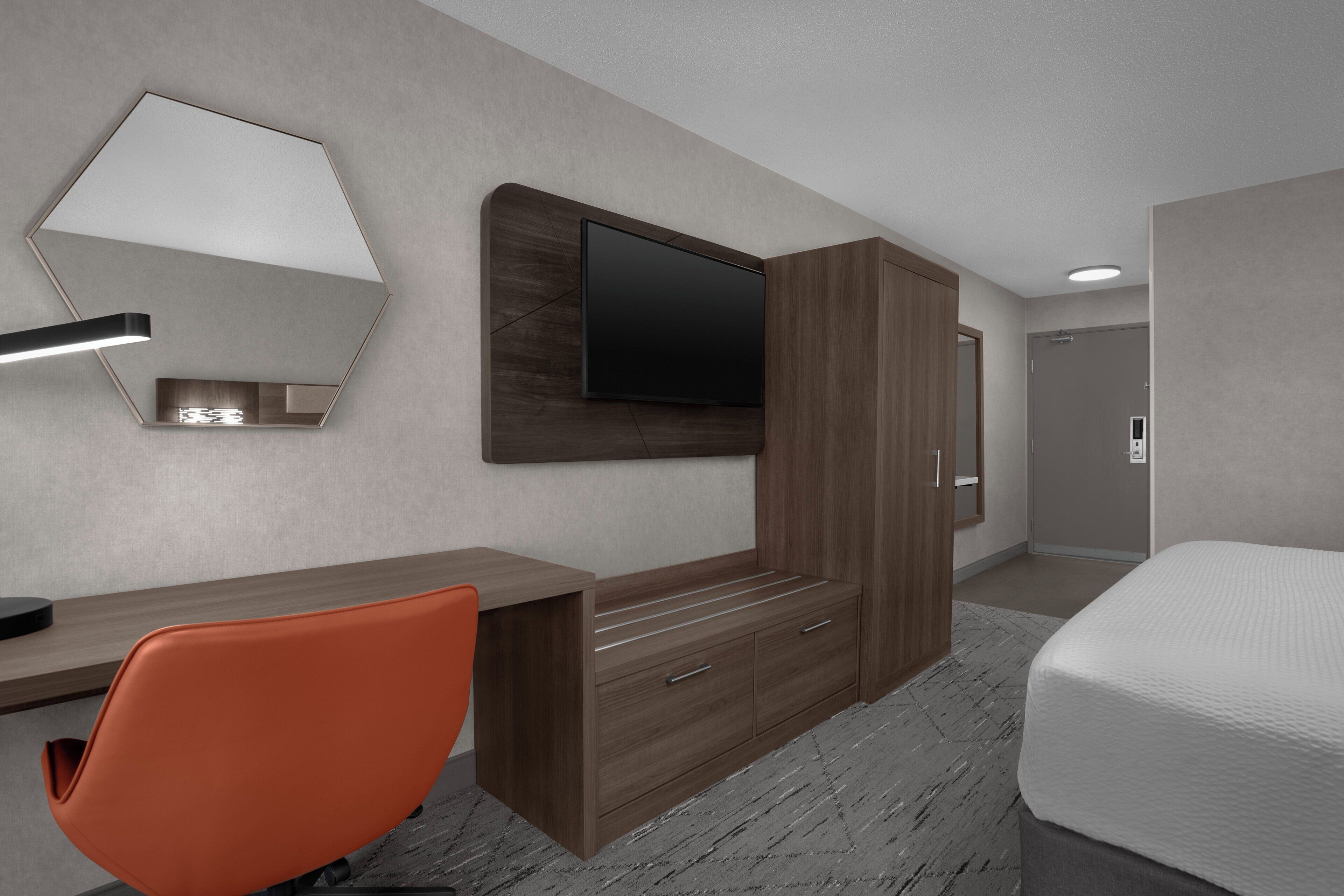 A modern hotel room with a large bed, a desk with a chair, a wardrobe, a flat-screen TV, and a mirror.