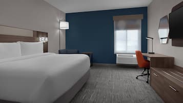 A hotel room with a large bed, a desk with a chair, a flat-screen TV, and a window with blinds.