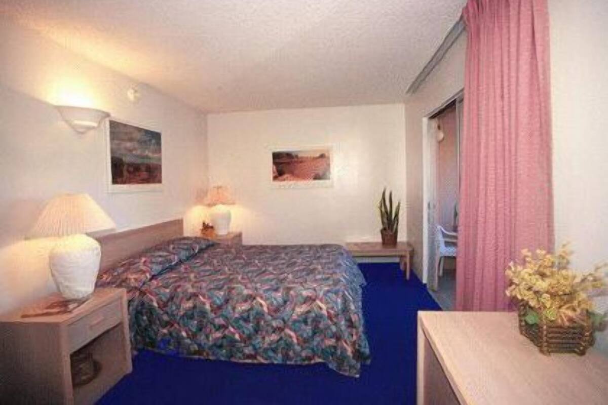 Une chambre d’hôtel avec un lit, une table de chevet avec une lampe, une petite table avec un vase et une chaise.