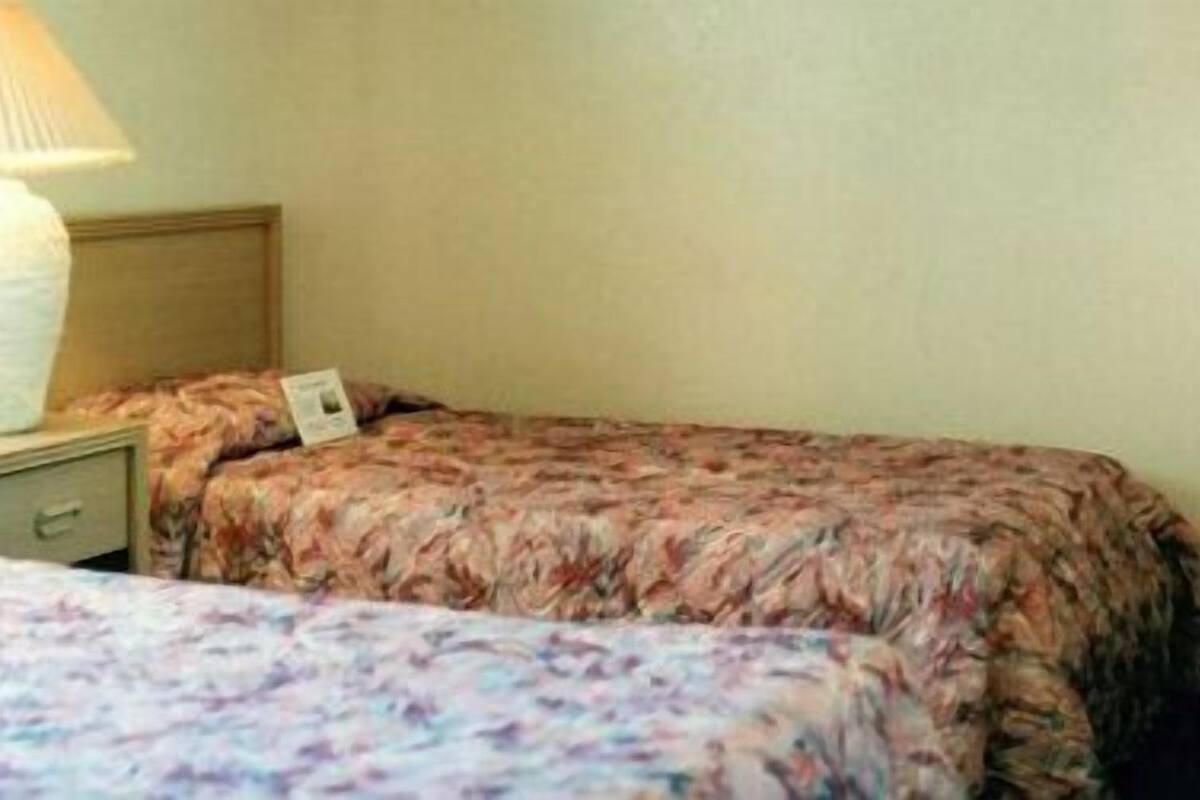 Une chambre d’hôtel avec deux lits, une table de chevet, une lampe et un téléphone fixé au mur.